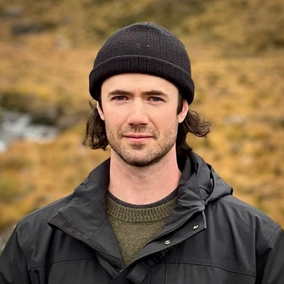 Image of Anthony standing in the Scottish Highlands wearing a black beanie and a smirk.